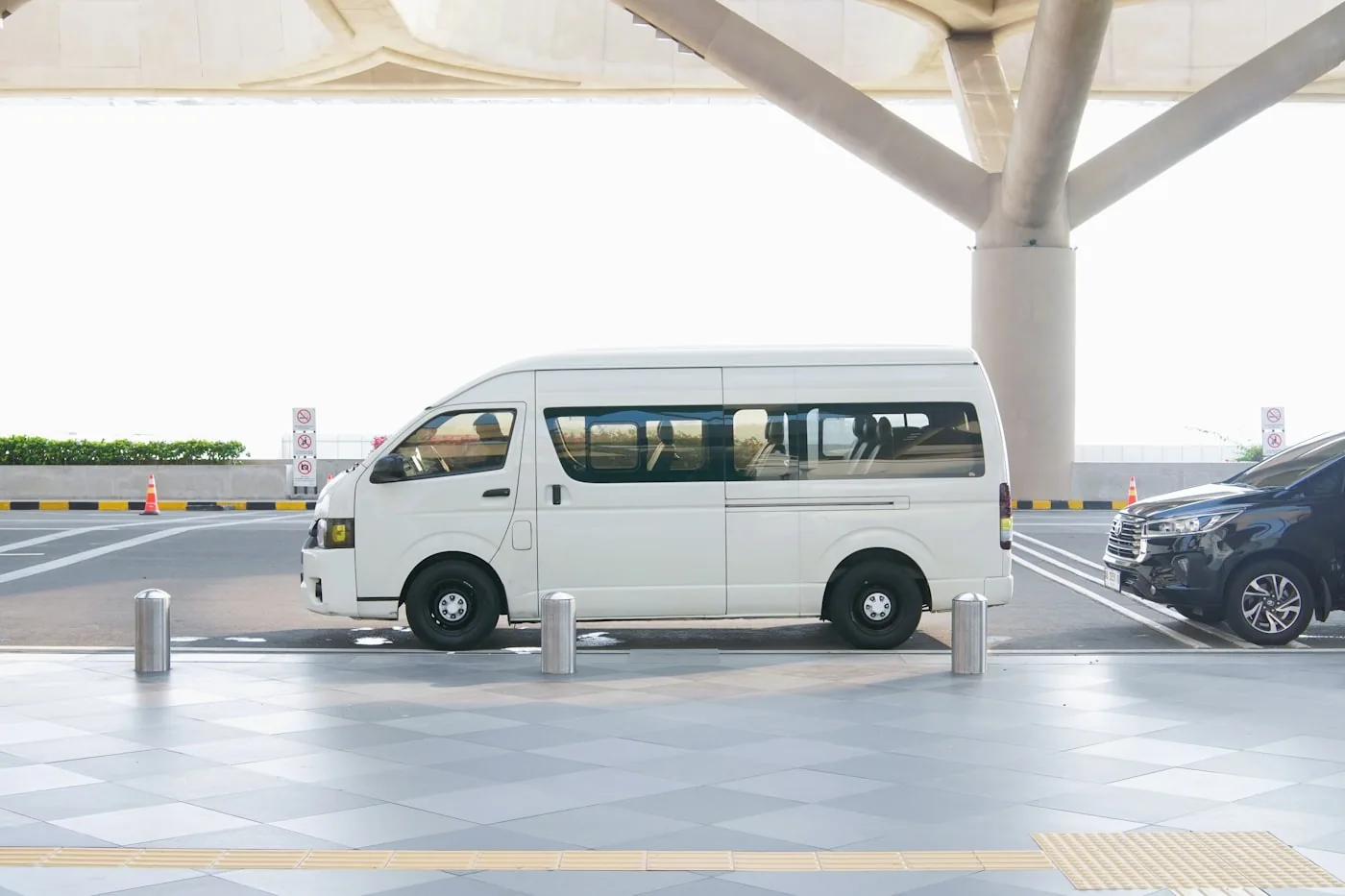 A passenger van parked at an airport terminal curb for a transfer pickup
