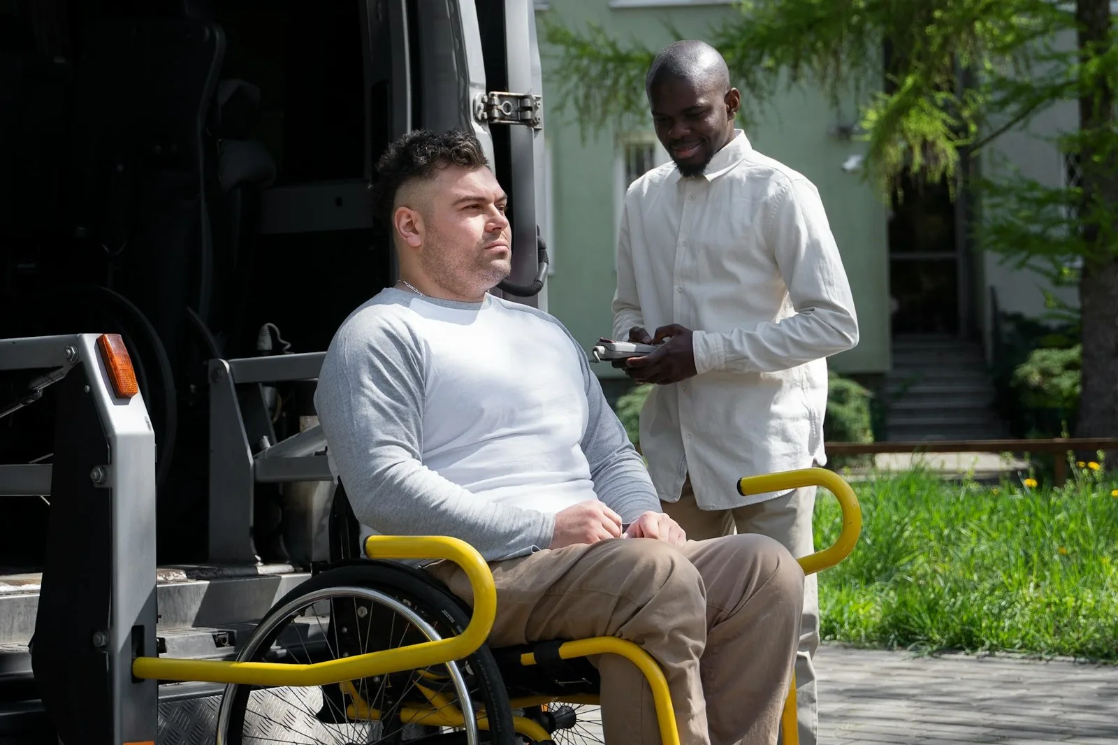 A Larkspur Mobility driver assisting a wheelchair user from the van's accessibility lift outside a residence