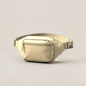 Birch Hip Pack in Sand — compact hip pack with a zipped front pocket and a buckled waist strap on a light grey backdrop