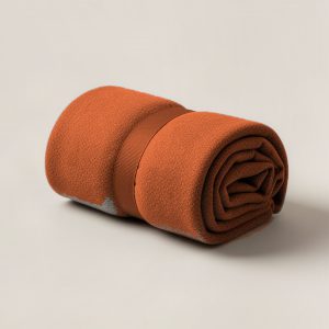 Cedar Camp Throw in Rust — soft camp throw blanket, rolled with a strap on a light grey backdrop