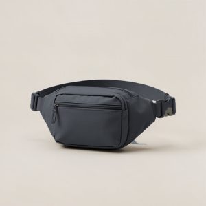 Cedar Hip Pack in Charcoal — compact hip pack with a zipped front pocket and a buckled waist strap on a light grey backdrop
