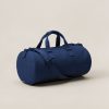 Driftwood Duffel in Navy — cylindrical duffel bag with carry handles and a shoulder strap on a light grey backdrop