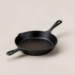 Ember Cast Iron Skillet — black seasoned cast iron skillet with a loop helper handle on a light grey backdrop