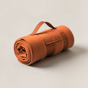 Ember Stadium Blanket in Rust — compact stadium blanket, rolled with a carry strap on a light grey backdrop
