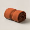 Harbor Camp Throw in Rust — soft camp throw blanket, rolled with a strap on a light grey backdrop