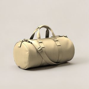 Juniper Duffel in Sand — cylindrical duffel bag with carry handles and a shoulder strap on a light grey backdrop