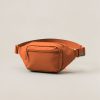 Ridgeline Hip Pack in Rust — compact hip pack with a zipped front pocket and a buckled waist strap on a light grey backdrop