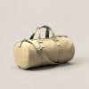 Summit Duffel in Sand — cylindrical duffel bag with carry handles and a shoulder strap on a light grey backdrop