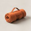 Trailhead Stadium Blanket in Rust — compact stadium blanket, rolled with a carry strap on a light grey backdrop