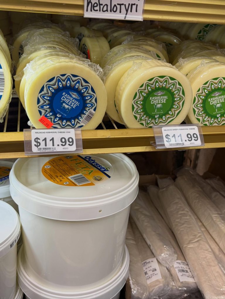 Wheels of white cheese and feta in the cooler, with a Metalotyri sign