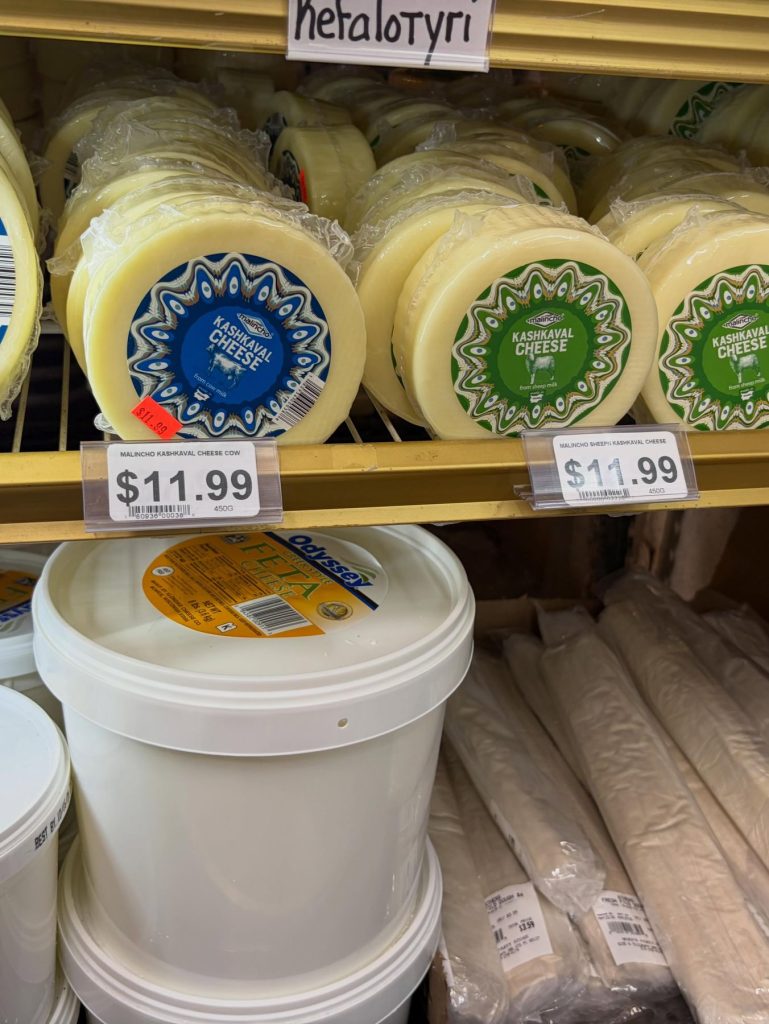 Wheels of white cheese and feta in the cooler, with a Metalotyri sign