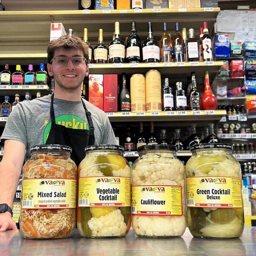 Team member at the counter with big jars of Vava mixed salad, vegetable cocktail and cauliflower